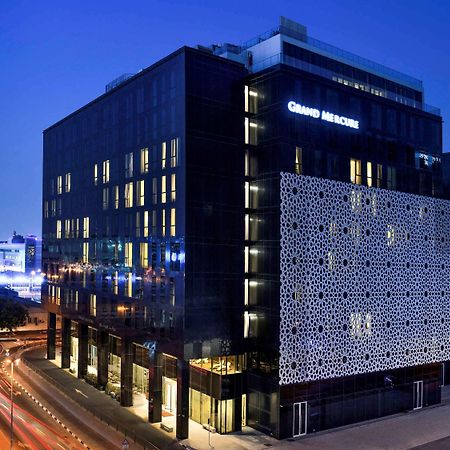 Grand Mercure Dubai City Exterior foto The photo shows a modern building at night, featuring a sleek, contemporary design. The building has a large facade with a distinctive patterned wall on one side. Illuminated signs display the name "Grand Maison." Surrounding the building, there are 