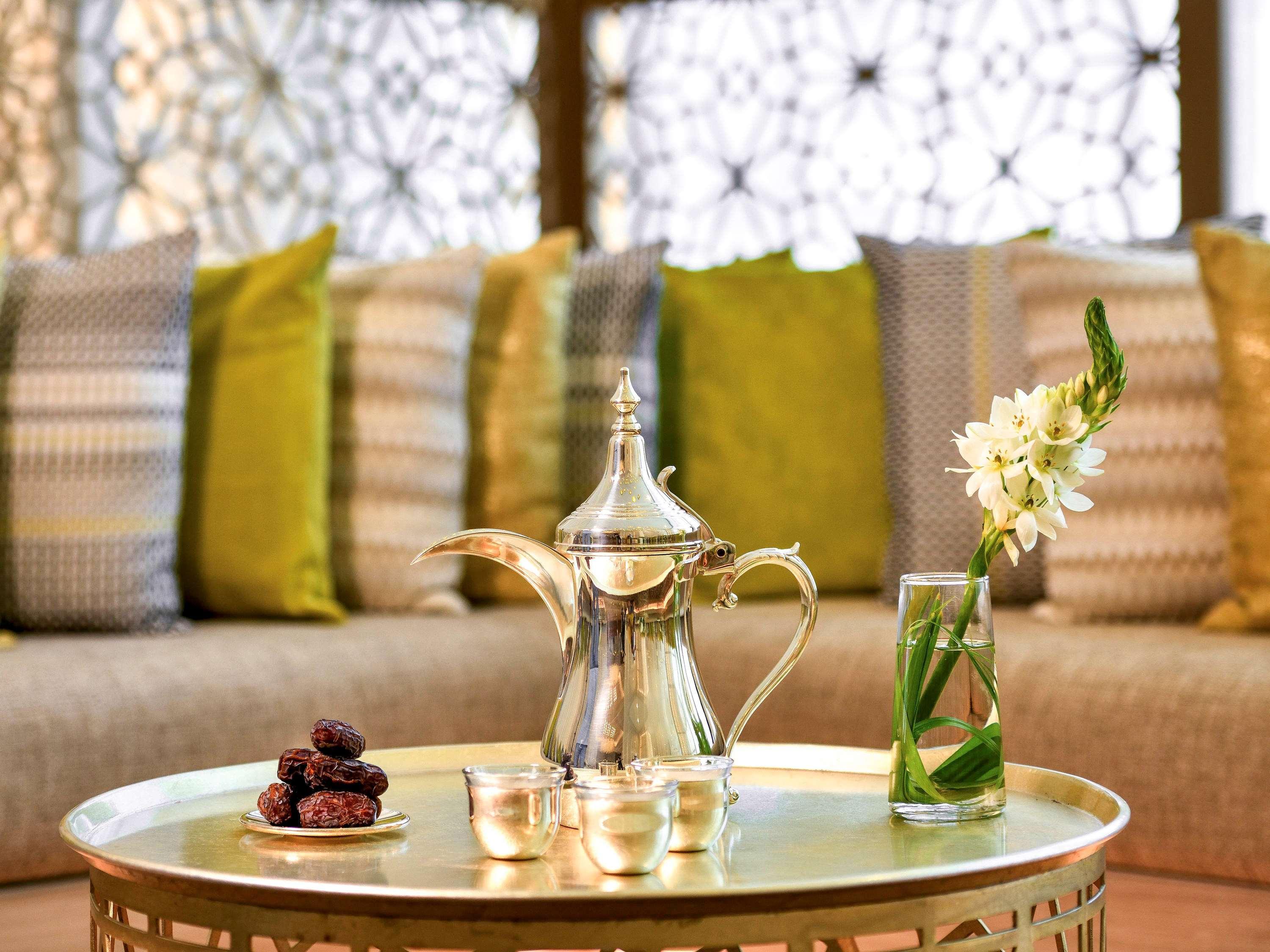 Grand Mercure Dubai City Exterior foto The photo features a decorative table with a shiny silver coffee pot and a small set of cups, indicating a traditional beverage service. Around the pot, there are some dates placed on a small dish. In addition, a clear glass vase holds a few green st