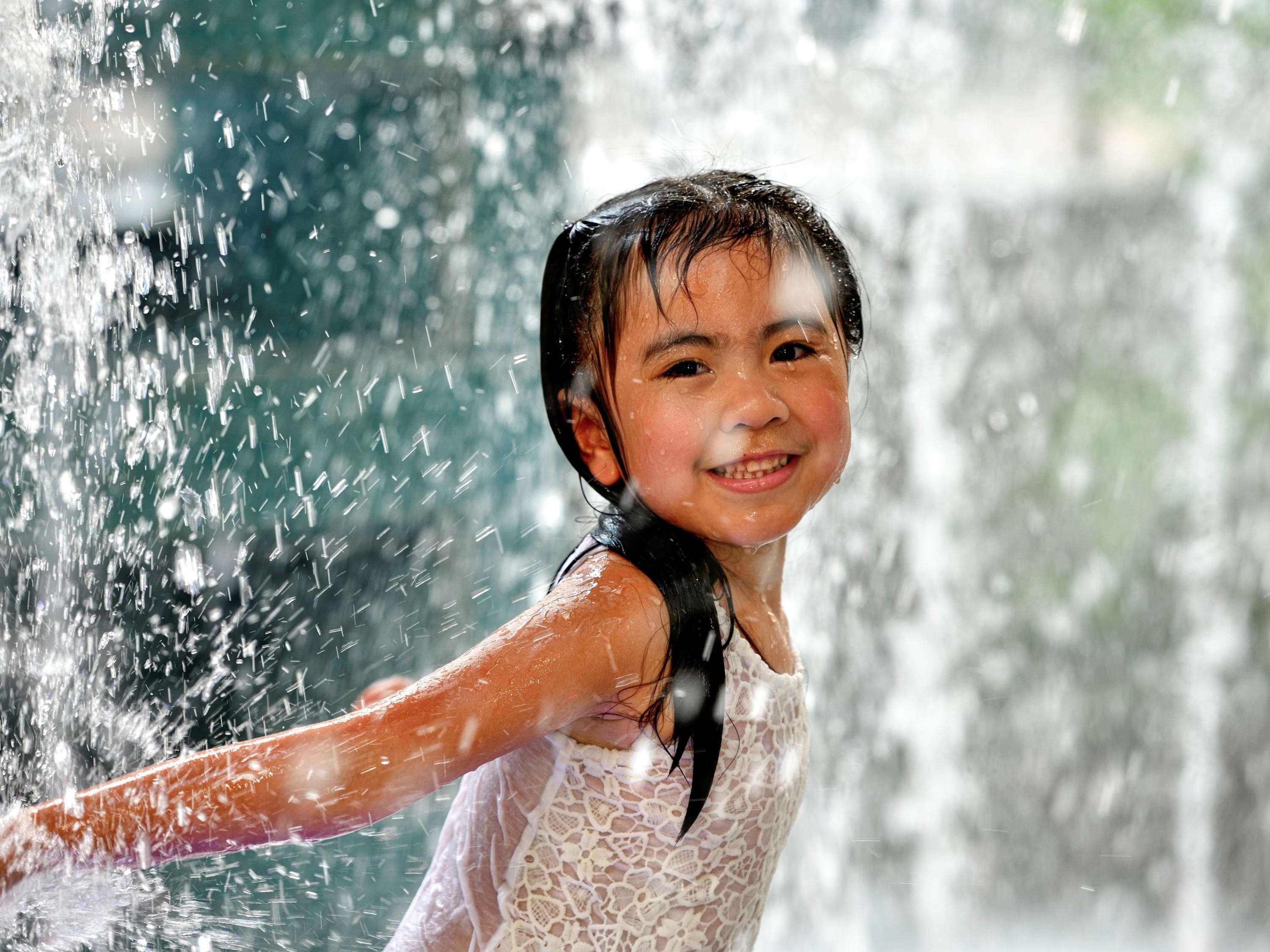 Grand Mercure Dubai City Exterior foto The photo shows a young girl joyfully playing in a water fountain. She has wet hair and is wearing a light-colored outfit, possibly a dress or swimsuit. The background features splashes of water cascading down, creating a refreshing and playful atmos