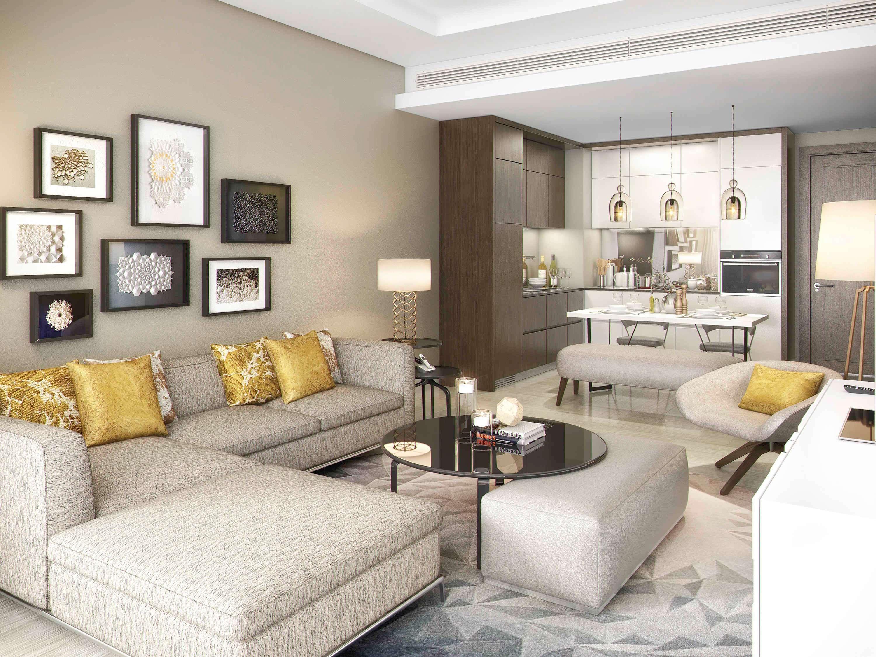 Grand Mercure Dubai City Exterior foto The photo shows a modern living room and kitchen area. The living room features a light-colored sectional sofa with decorative pillows in shades of gold. There is a round black coffee table placed in front of the sofa. On the wall, there are several 