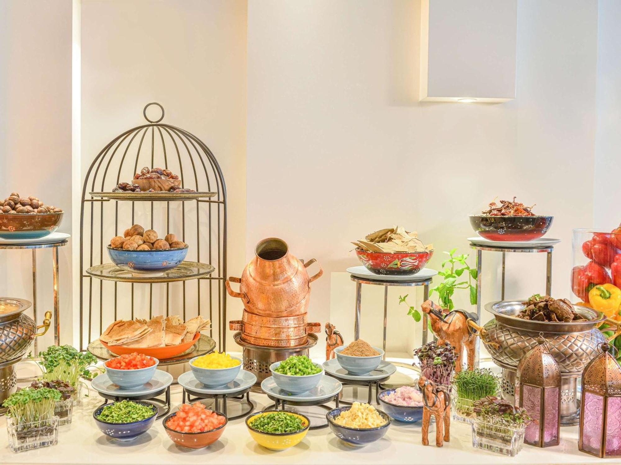 Grand Mercure Dubai City Exterior foto The photo displays a beautifully arranged buffet setup featuring an assortment of dishes. There are several bowls in various colors filled with different ingredients, including grains, herbs, and toppings. A decorative cage holds additional food item